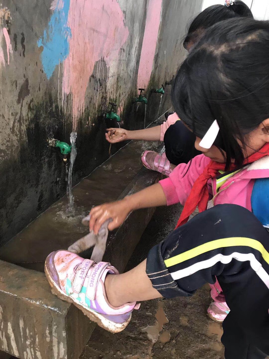 这里刚下过雨,山路泥泞,早上到校的孩子在水池旁洗着鞋,洗掉泥巴后