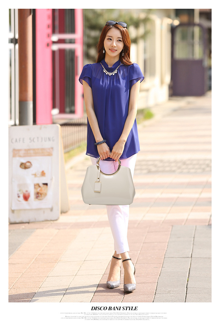 Glossy patent leather handbag, cream, being held by a woman walking down the street