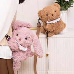 春の幼稚園の熊が腹ばいになってウサギのリュックサックのぬいぐるみを包んでいます。