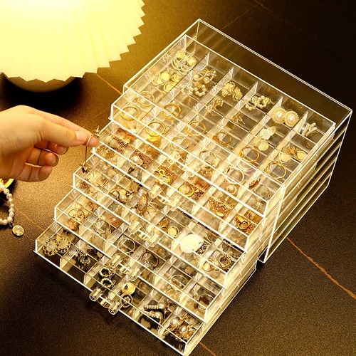 A transparent jewelry box with compartments for earrings, necklaces, rings, and beads