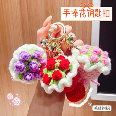 毛糸の手に花のひまわりのキーホルダーのペンダントを飾って、バラの手作りの編みインスタ風のカバンを飾ってアクセサリーを掛けます。