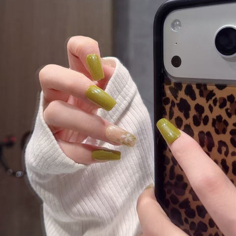 Forest-style artistic olive green patchwork press-on nails with a translucent base color, white floral patterns, and polka dots, creating an atmospheric short nail look