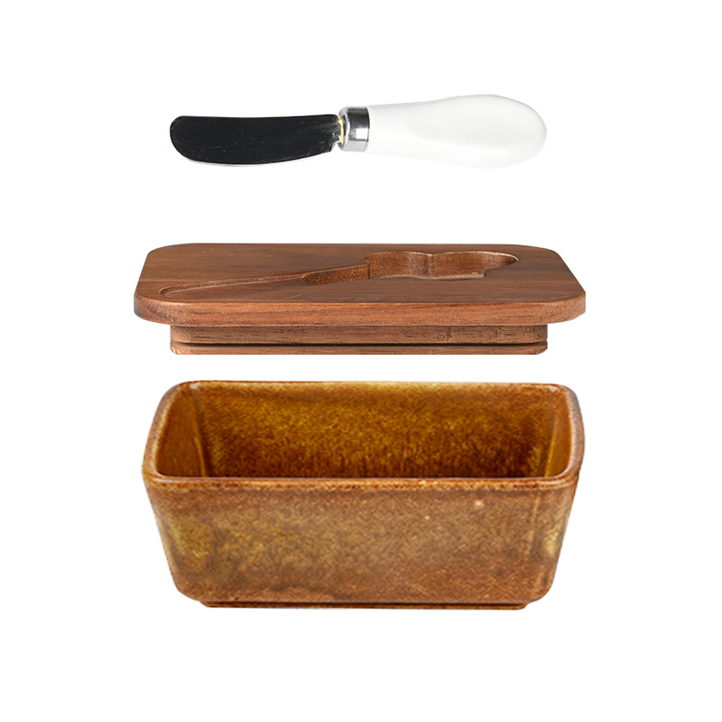 Mantequillera de cerámica con tapa de madera y cuchillo, apta para uso alimentario.