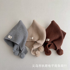 赤ちゃんのかわいいコーヒー色の耳保護キャップの太いニットの広い縁に毛玉の子供の先の暖かい毛糸の帽子がついています。