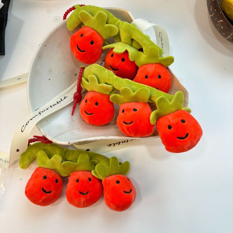 かわいい串刺しのトマトのほほえみの果物の表情の包みのぬいぐるみの公の子の包みのペンダントのゲーム城は子供機のプレゼントをつかみます。|undefined