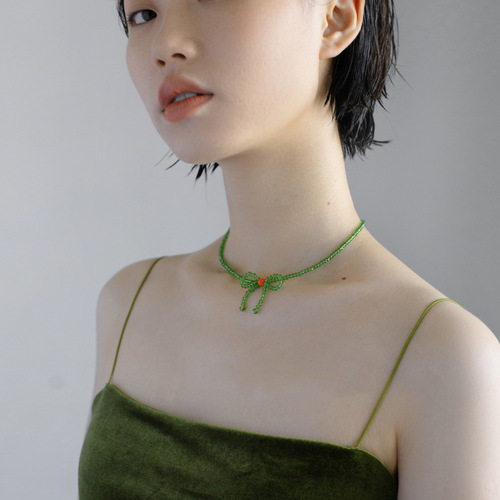 A minimalist and stylish green butterfly knot necklace for women, featuring small, fresh and elegant glass crystal beads, designed as a choker or lockchain.