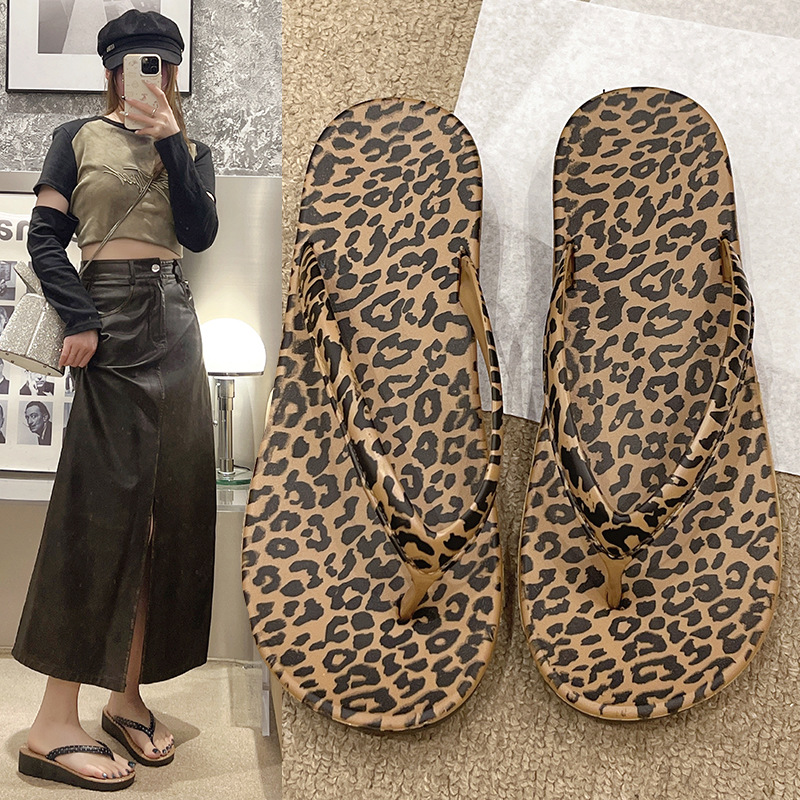 En verano de 2025, las nuevas zapatillas de estilo leopardo de fondo plano y moda son antideslizantes y las mujeres usan zapatillas frías con pendientes de pies de playa.