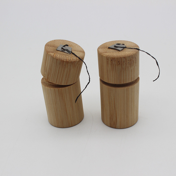 Two light brown bamboo floss tube portable biodegradable cases with black string and metal clips for convenient storage and use.