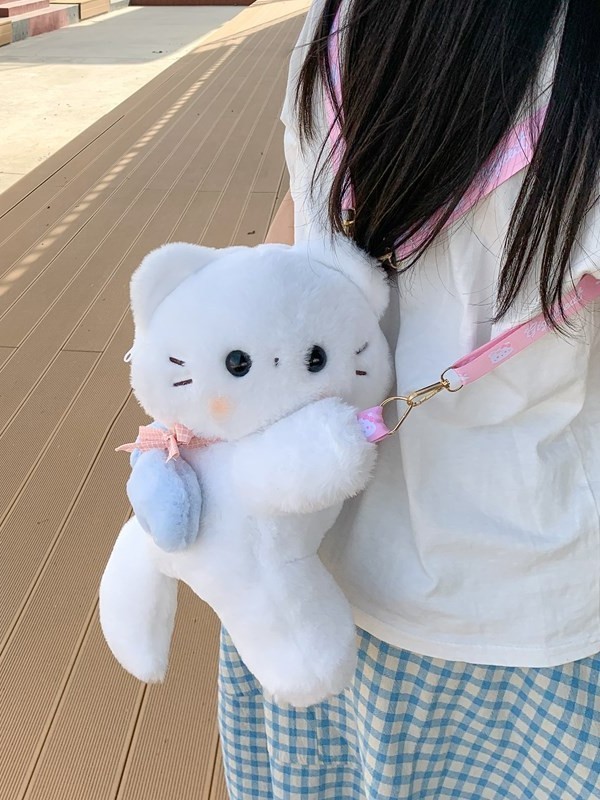 天使の子猫が腹ばいになってランドセルのショルダーバッグ2025の新型のかわいい女の子の毛のふわふわしているリュックサックが寝ている子供を抱いています。|undefined