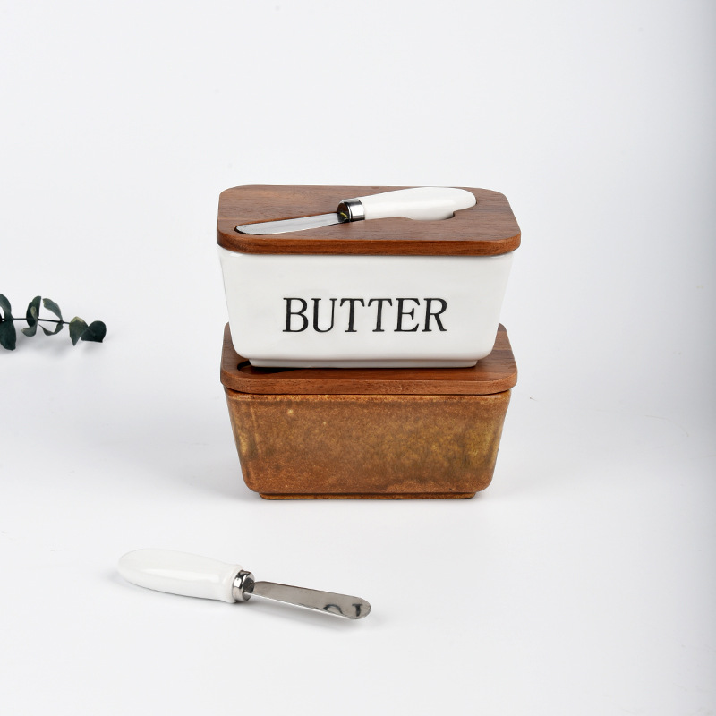 Mantequillera de cerámica con tapa de madera y cuchillo, apta para uso alimentario.