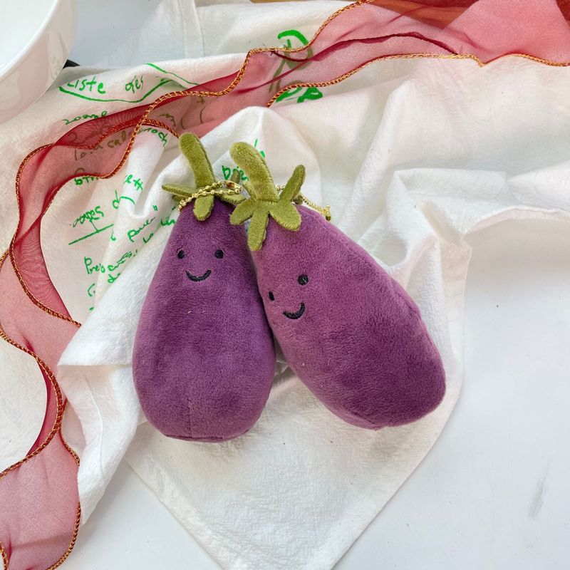 かわいい超萌えナスのほほえみ野菜の表情はぬいぐるみの息子の包みのペンダントのゲーム城を包んで子供のプレゼントをつかみます。|undefined