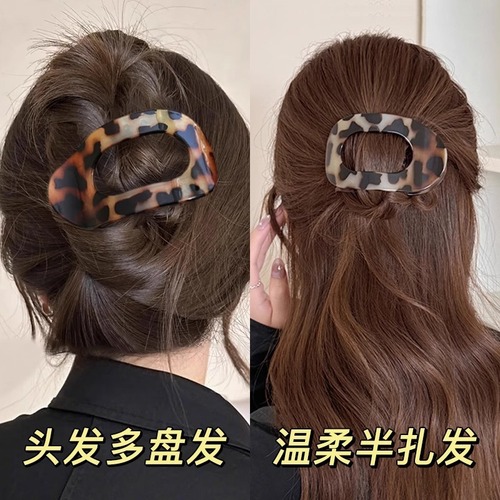Shellfish-shaped hair clip with a round, flat back, designed to clip onto a woman's full, rounded hair bun, featuring an arched tail hair clip as a head accessory.