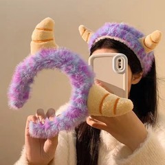 漫画のカラフルな紫色の牛の角のカチューシャのぬいぐるみの小さい怪獣の顔を洗って髪をつけます。