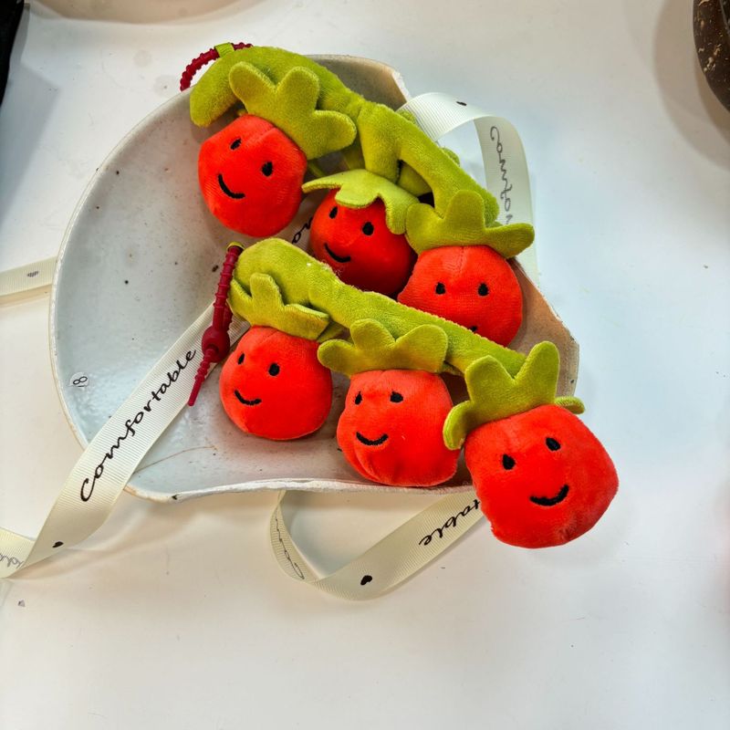 かわいい串刺しのトマトのほほえみの果物の表情の包みのぬいぐるみの公の子の包みのペンダントのゲーム城は子供機のプレゼントをつかみます。|undefined