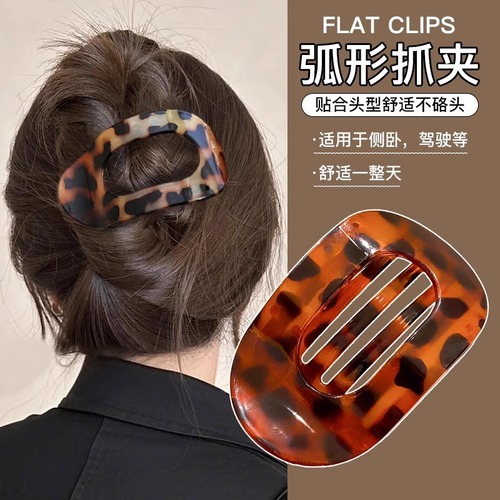 Shellfish-shaped hair clip with a round, flat back, designed to clip onto a woman's full, rounded hair bun, featuring an arched tail hair clip as a head accessory.