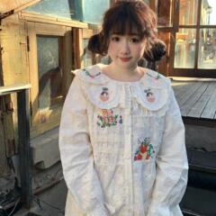 早春の甘くて可愛い女の子の刺繍花びらが長袖のシャツをめくっています。