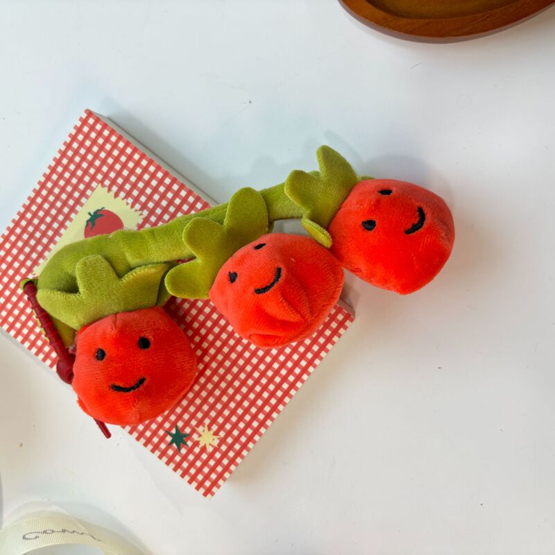かわいい串刺しのトマトのほほえみの果物の表情の包みのぬいぐるみの公の子の包みのペンダントのゲーム城は子供機のプレゼントをつかみます。|undefined