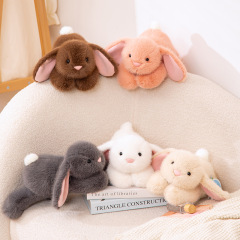 うつ伏せ姿の艾吉兎のぬいぐるみの子供はかわいい耳を垂れたウサギのぬいぐるみのプレゼントに付き添ってぼんやりしています。