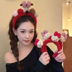 新年の秋冬のぬいぐるみの蝶結びのかわいい熊の子犬のカチューシャの少女の顔を洗ってマスクを塗って髪のカチューシャを押します。