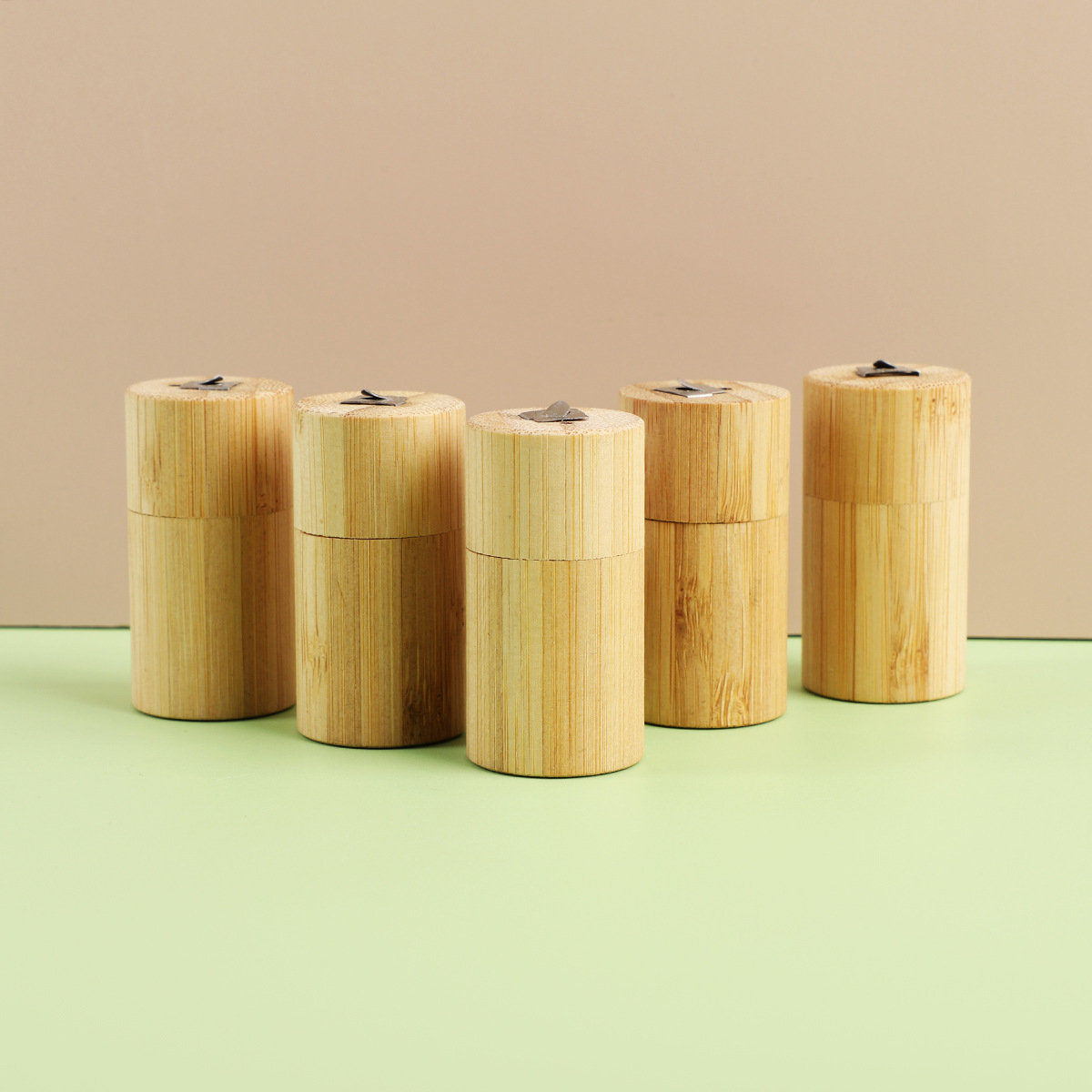 Five light brown bamboo cylindrical portable biodegradable floss tubes with metallic lids displayed together.