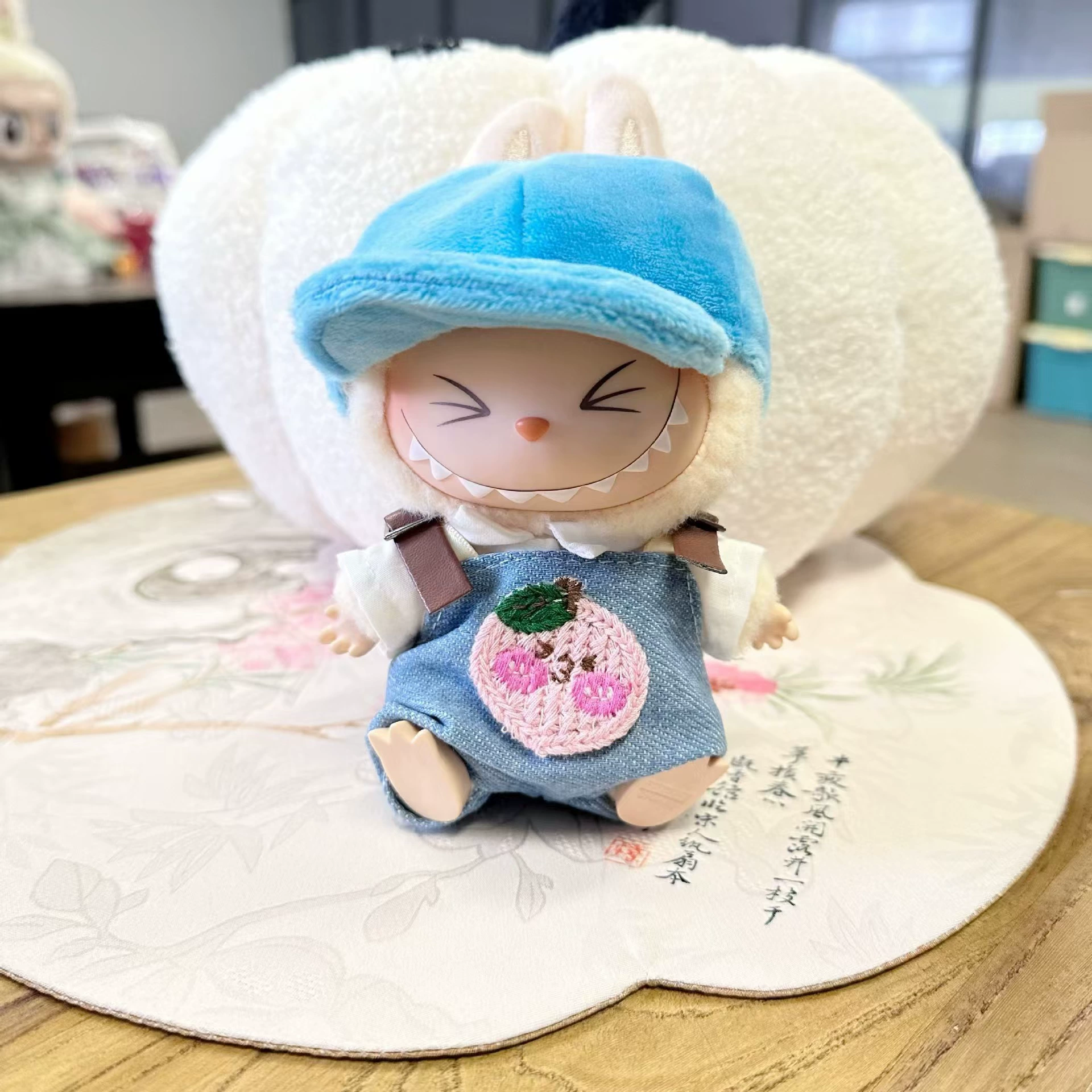 Лабубу Labubu сидит в джинсах, fisherman's шляпа, одет в милые простые детские наряды