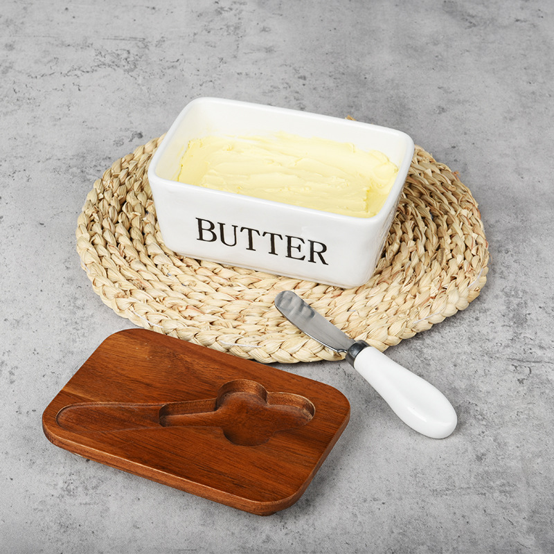 Mantequillera de cerámica con tapa de madera y cuchillo, apta para uso alimentario.