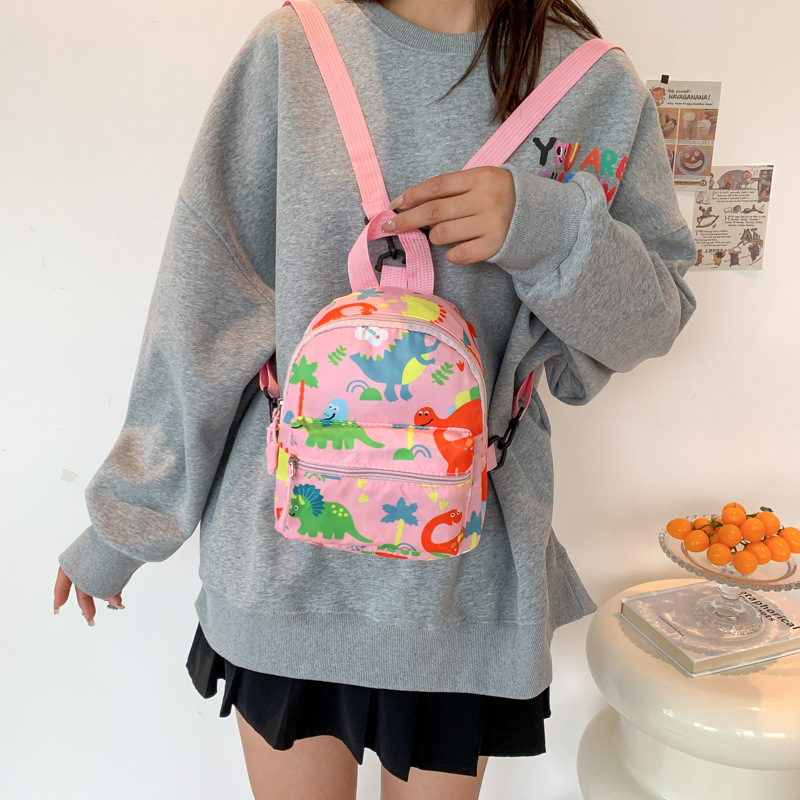 Mochila nueva al por mayor 2025, mochila de tela Oxford con diseño de dinosaurio de dibujos animados, mochila pequeña de gran capacidad para actividades al aire libre y ocio.