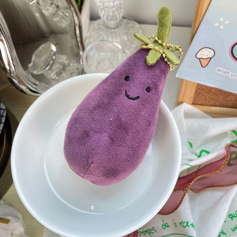 かわいい超萌えナスのほほえみ野菜の表情はぬいぐるみの息子の包みのペンダントのゲーム城を包んで子供のプレゼントをつかみます。|undefined