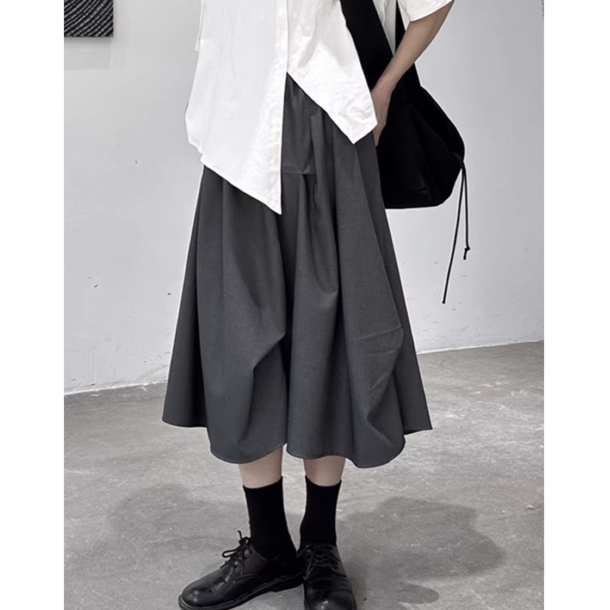 A stylish black Amber Ma-inspired little black dress with an asymmetrical design, featuring a unique high waist and pleats, perfect for spring.